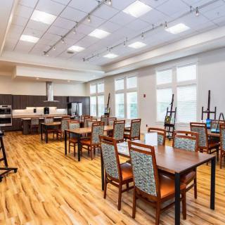 A spacious, brightly lit dining area with multiple tables and chairs, adjacent to a kitchen.