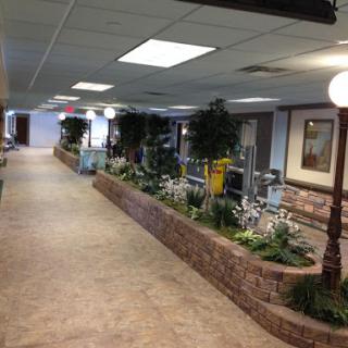 A well-lit indoor hallway featuring decorative plants and a brick landscaping element.