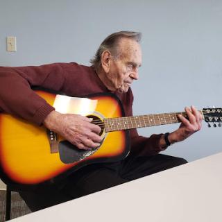 An elderly man passionately playing an acoustic guitar.