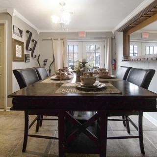A stylish dining room featuring a dark wooden table set with plates and decor, surrounded by elegant chairs and illuminated by overhead lighting.