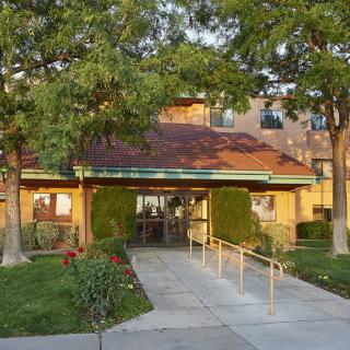 A building entrance with a pathway lined by trees and shrubs.