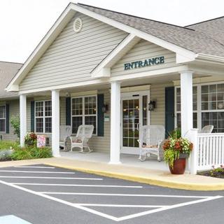 A suburban building entrance with a porch, chairs, and potted plants.
