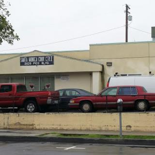 A view of a commercial building with multiple red vehicles parked in front on a cloudy day.