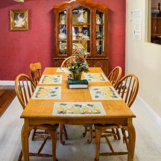 A cozy dining room with a wooden table and chairs, set against a warm red wall with a china cabinet in the background.