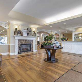 A spacious, elegantly decorated lobby with a wooden floor, fireplace, and central table with plants.