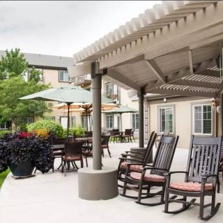 A serene patio area with rocking chairs and a pergola, overlooking a garden in a residential setting.