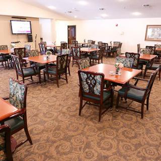 A spacious dining room featuring multiple tables and chairs, with a patterned carpet and warm lighting.
