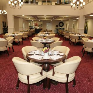 Elegant dining room with neatly arranged tables and chairs, featuring a red carpet and chandeliers.