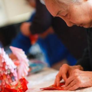 An elderly person carefully folding origami paper, focusing on their intricate craft.