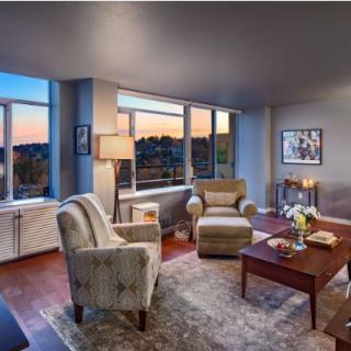 A cozy living room with armchairs, a coffee table, and large windows overlooking a sunset.
