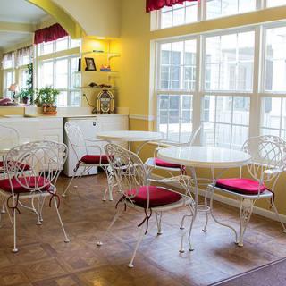 A cozy dining area with white tables and chairs, featuring red cushions and large windows.