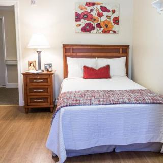 A cozy bedroom with a neatly made bed, wooden nightstand, and decorative painting.