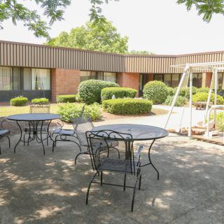 A peaceful courtyard with patio tables, chairs, and a swing surrounded by greenery.
