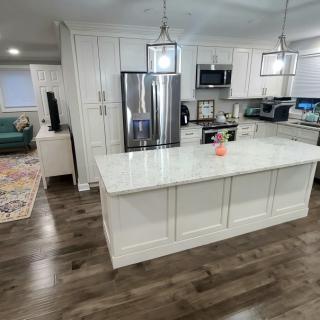 A modern kitchen with white cabinets, a central island, stainless steel appliances, and pendant lighting.
