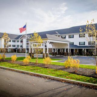 A large building with an American flag, surrounded by landscaped greenery and a driveway under a cloudy sky.