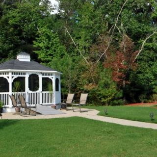 A serene outdoor setting featuring a white gazebo and lounge chairs surrounded by lush greenery.