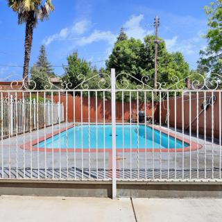 An outdoor swimming pool surrounded by a fence with trees and a clear blue sky in the background.