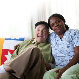 A caregiver and elderly person sitting together, sharing a joyful moment at home.