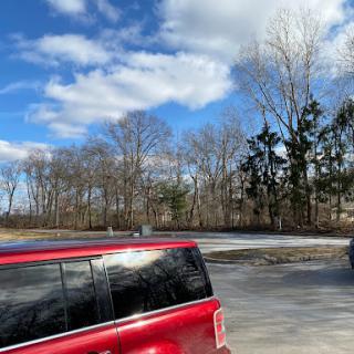 A red car parked outdoors under a partly cloudy sky with trees in the background.