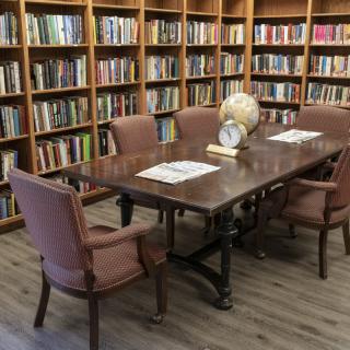 A cozy library reading room with a wooden table surrounded by chairs and bookshelves.