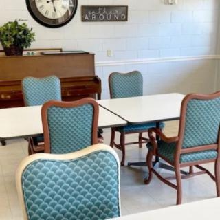 A room with blue upholstered chairs, tables, a piano, and a wall clock.
