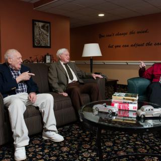 A group of elderly men sitting and conversing in a comfortable living room setting.