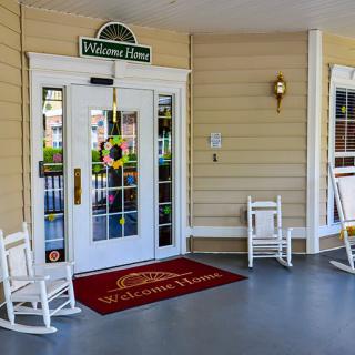 A cozy porch entrance features a welcome mat, double doors, and rocking chairs.