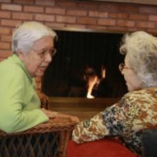Two elderly individuals engaged in a conversation by the fireplace.