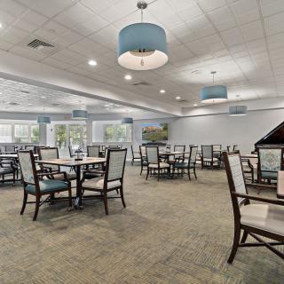 A spacious dining room with neatly arranged tables and chairs, featuring modern ceiling lights and large windows.
