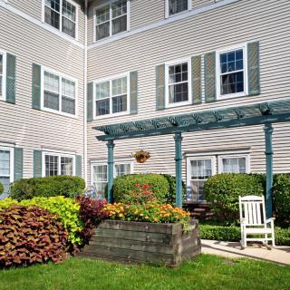 A well-maintained garden area in front of an apartment building with a bench and lush greenery.