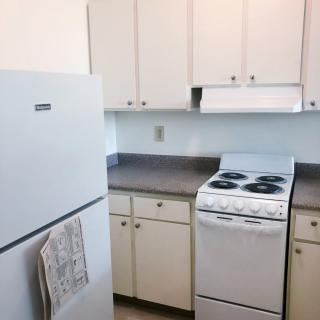 A compact kitchen with a refrigerator, stove, and white cabinets.