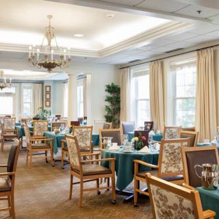Elegant dining room with neatly arranged tables and chairs, complemented by chandeliers and large windows.