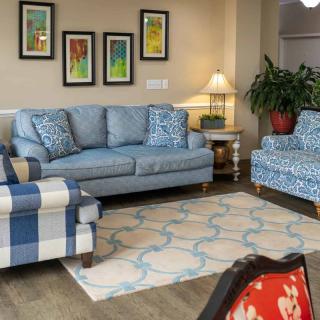 A cozy living room featuring a blue sofa and armchair, complemented by colorful paintings and a patterned rug.