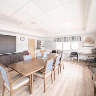 A spacious and well-lit meeting room featuring a large table surrounded by chairs, suitable for collaborative work.