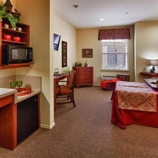 A cozy bedroom interior featuring a bed, desk, and small kitchenette.
