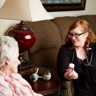 A nurse is talking to an elderly woman during a home visit, holding a bottle of medication.