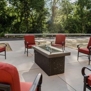An inviting outdoor patio with red cushioned chairs surrounding a central fire pit, set against a backdrop of lush trees.