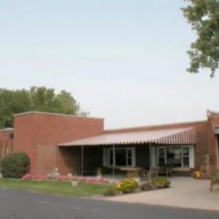 A brick building with a covered entrance, surrounded by trees and landscaping.