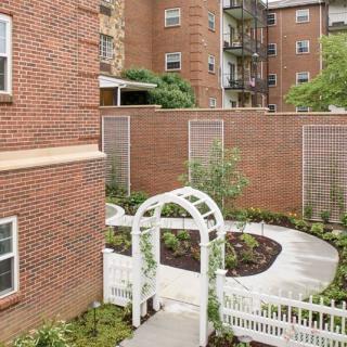 Urban garden with a white archway and landscaped path surrounded by brick buildings.