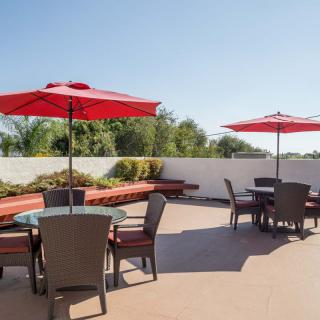 A sunny outdoor patio with tables and red umbrellas.