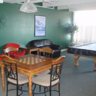 A cozy game room featuring a pool table, chessboard, sofa, and table with chairs against a green wall.