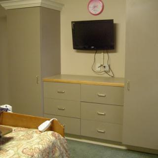 A cozy room featuring a television mounted on the wall, a dresser with drawers, and a wall clock.