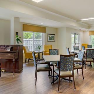 A bright dining area with tables, chairs, and a piano.