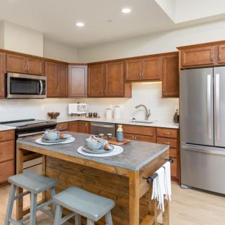 A modern kitchen featuring a central island with stools, stainless steel appliances, and wooden cabinetry.
