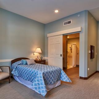A cozy bedroom with blue walls and a single bed, featuring a lamp, chair, and side table.