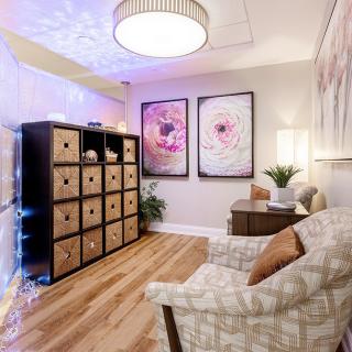 A cozy living room with stylish decor, featuring an armchair, shelving unit, and framed artwork on the walls.