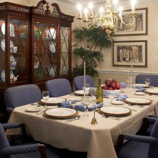 A formal dining room set for an elegant dinner, featuring a chandelier, china cabinet, and candles.