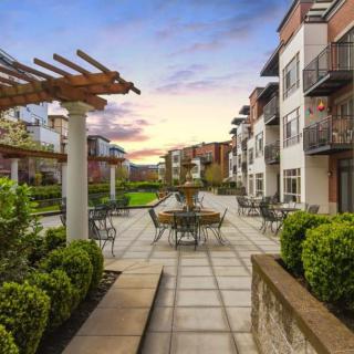 A modern apartment complex featuring an inviting outdoor patio with seating areas, beautifully landscaped and set against a stunning sunset backdrop.