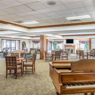A spacious, well-lit room featuring a piano, several tables and chairs, and large windows.