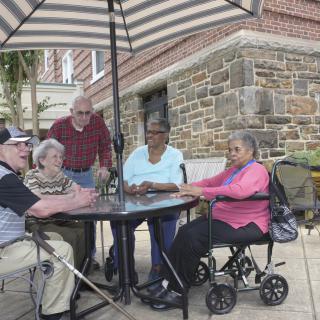 A group of elderly individuals socializing outdoors under a striped umbrella.